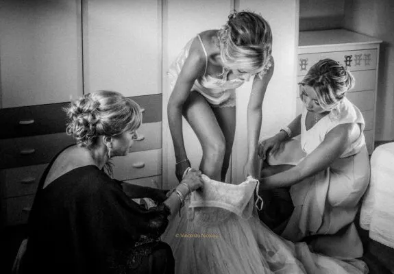 Fotografo di matrimonio in Sicilia durante la preparazione della sposa aiutata dai familiari a indossare l'abito prima della cerimonia.
