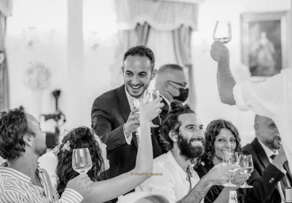 Fotografo di matrimonio in Sicilia fotografa lo sposo mentre brinda con gli amici durante il ricevimento, tra sorrisi, calici alzati e momenti spontanei di festa.