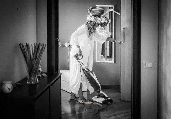 La sposa durante la preparazione mentre scherza passando l'aspirapolvere, raccontando un momento spontaneo e divertente prima della cerimonia.